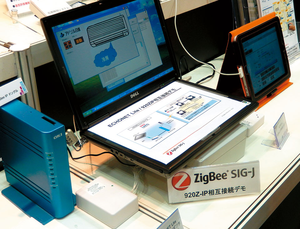 写真5　ZigBee SIG-J（SIGジャパン）のブースでは、沖電気、ラピスセミコンダクタ（LAPIS）、アドソル日進、テキサスインスツルメンツ（TI）が、①920MHzを使用しZigBee IP（920ZIP）を搭載したHEMSと、②エアコンや電力センサー（ともにECHONET Lite対応）を、ECHONET Liteミドルウェアアダプタを介して相互接続デモを展開した。電力センサーの情報を左側のタブレットに表示したり、擬似エアコン（パソコンで模擬）をタブレットから制御するなどのデモを行った。<br />
