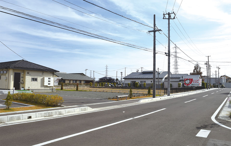 写真8　東北電力の送電線が通る電柱（右側）と東松島市の自営線が通る電柱（左）。エコタウンの集会所まで並行して2つの送電線が走る。高圧6,600Vの配電網（3相）。手前が集合住宅、その奥に見える屋根がわたなべ整形外科、電柱後ろの建物がししど内科クリニック。