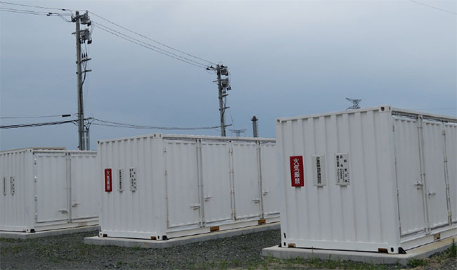 写真5　大容量蓄電池設備（リチウムイオン電池）と自営線の電柱（後方）