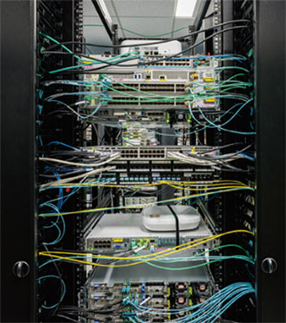 写真4　企業ネットワークを構成する機器等が設置されている。中央下の白いボックスは企業ネットワークでMEC（Mobile Edge Computing）を実現するENCS5400。その上の弁当箱のような機器は、Wi-Fi6対応のアクセスポイント（すべてシスコ製品）。