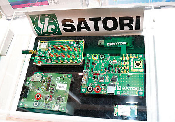 ▲佐鳥電機（株）（東京都港区）は、自社開発の920MHz無線モジュール（写真右下）と同モジュール搭載の評価ボード（写真右中央）、USBドングル（写真右上）を展示。Wi-SUNアライアンス方式対応のIEEE 802.15.4g（物理層）/4e（MAC層）を搭載し、そのネットワーク通信方式は、1対1通信、1対n通信、マルチホップ通信方式を備えている。現在は、サンプル出荷状態で、夏頃に出荷の予定。