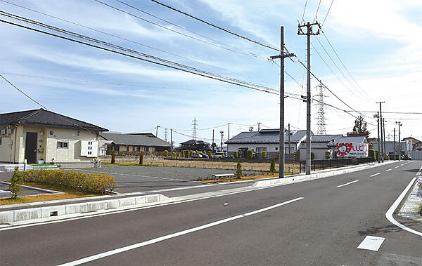 写真8　東北電力の送電線が通る電柱（右側）と東松島市の自営線が通る電柱（左）。エコタウンの集会所まで並行して2つの送電線が走る。高圧6,600Vの配電網（3相）。手前が集合住宅、その奥に見える屋根がわたなべ整形外科、電柱後ろの建物がししど内科クリニック。